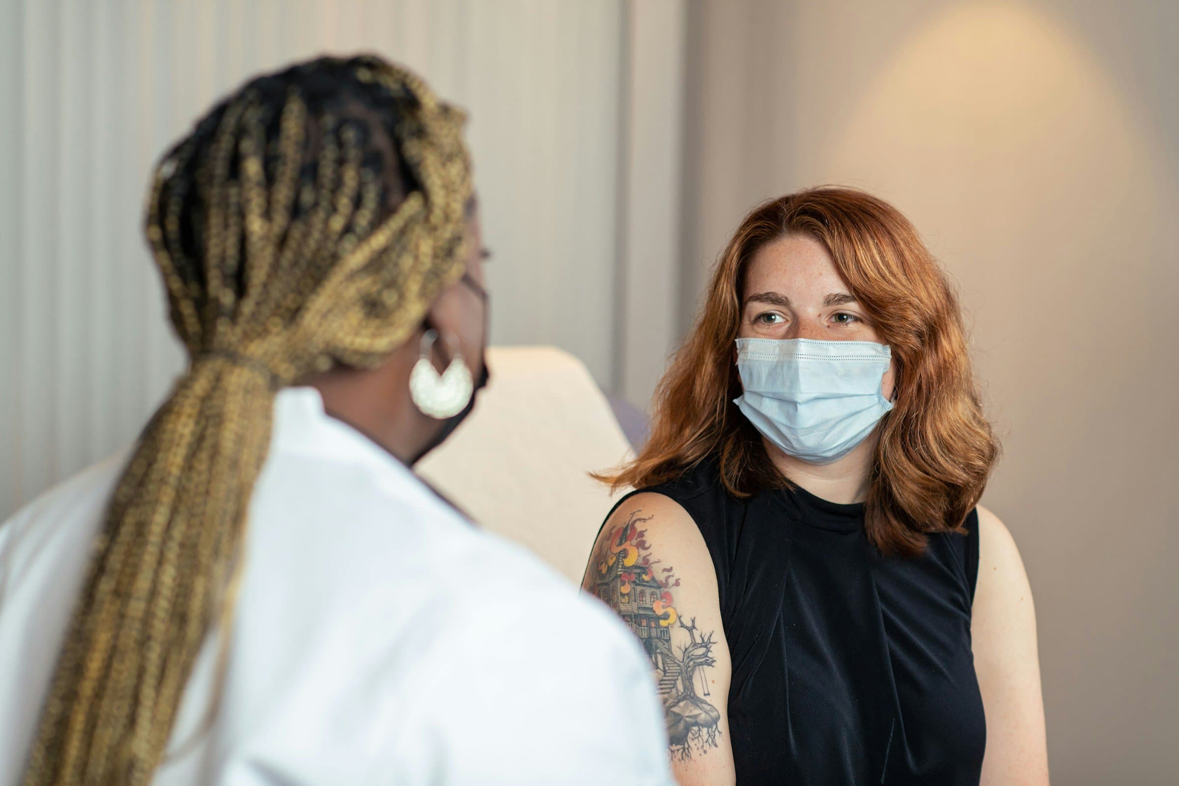 A clinician talks with a patient in a clinic room. Both wear masks.