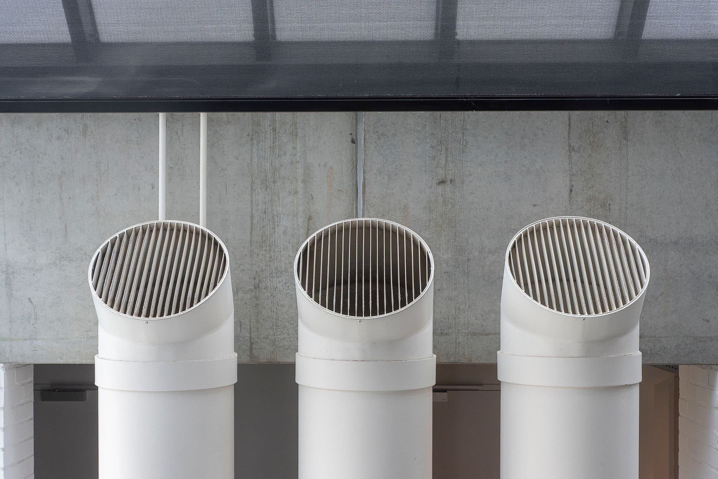 Three white ventilation intakes against a concrete wall.