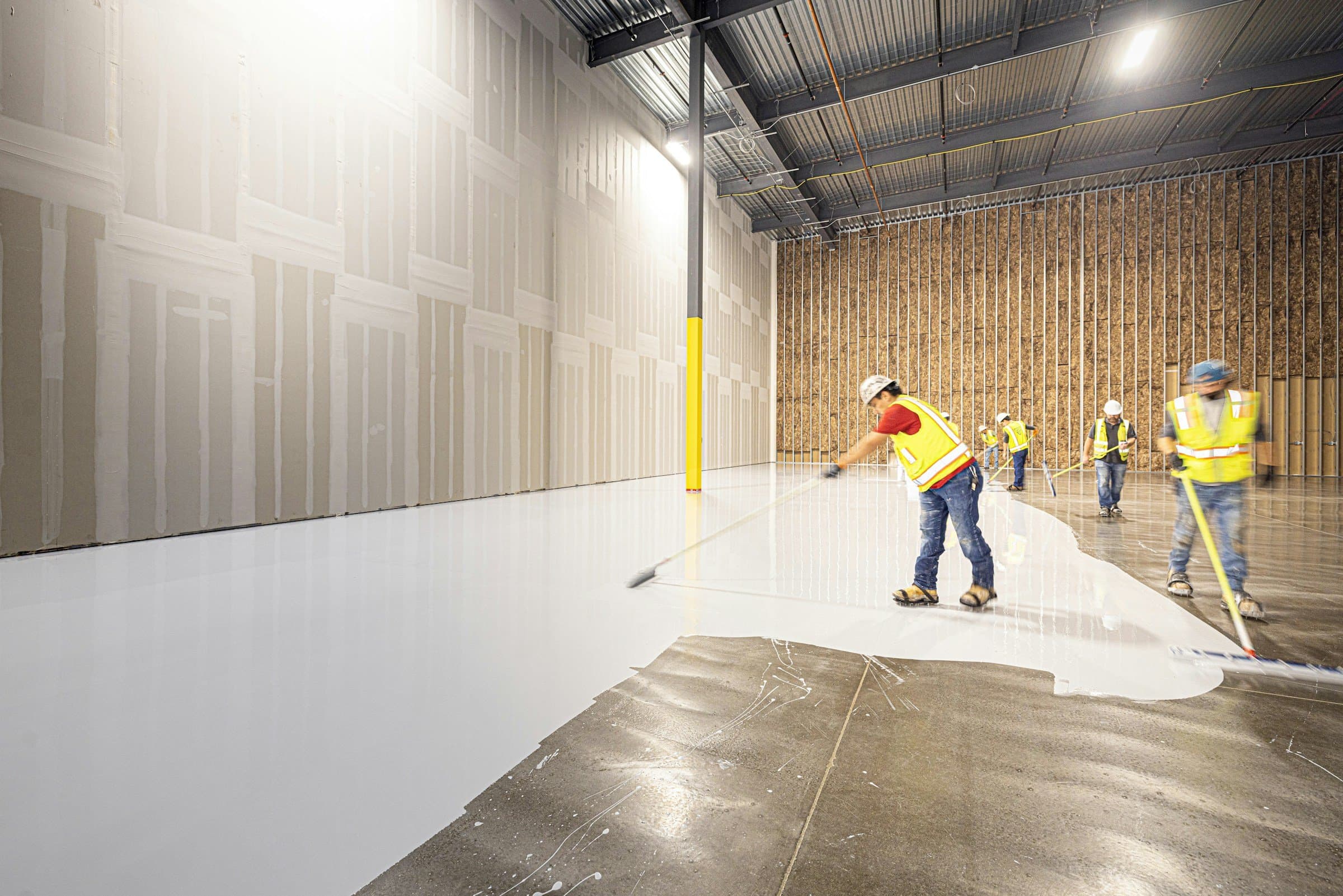A crew in safety vests coats the floor of a new warehouse.