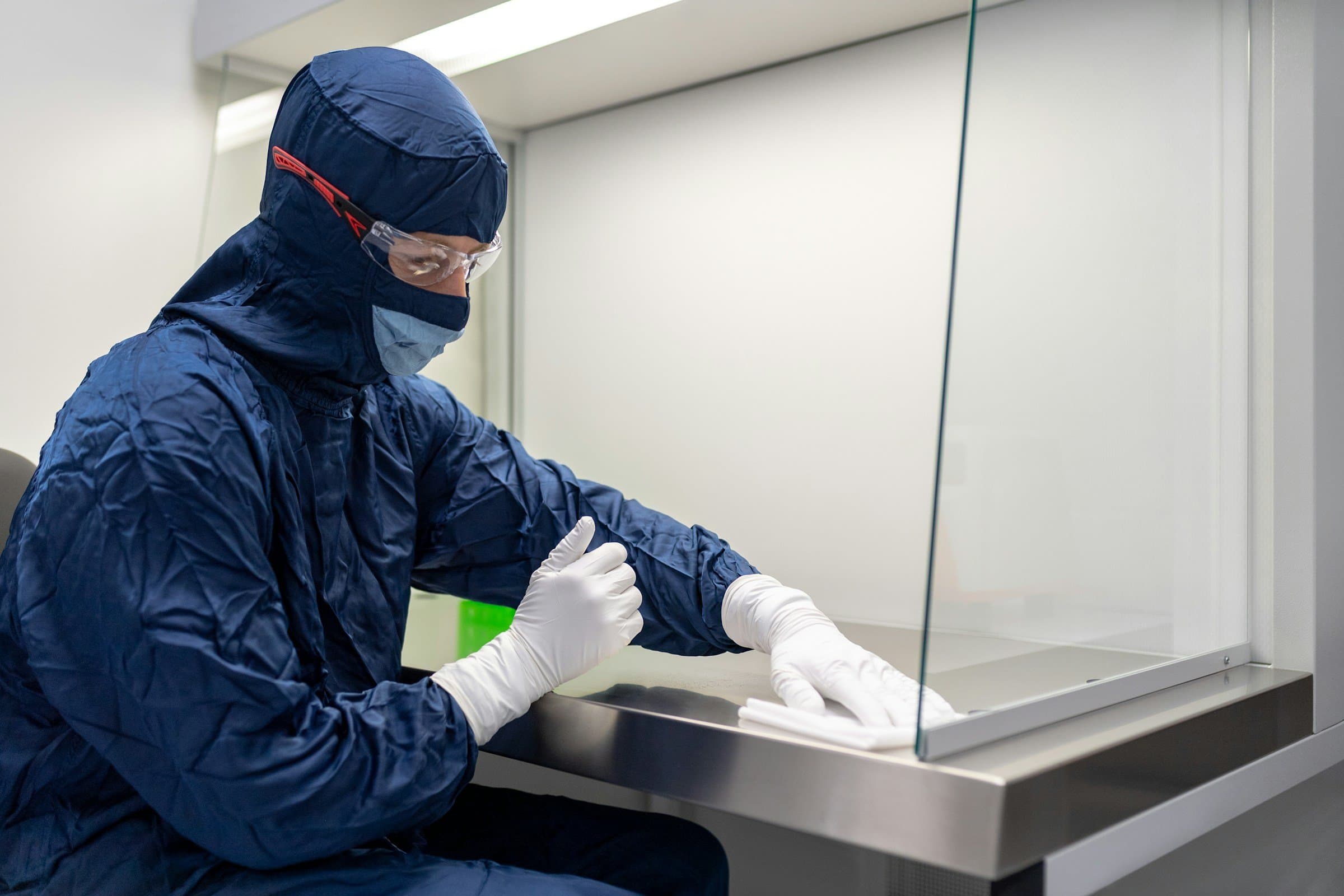 A technician in a cleanroom gown wipes down a laminar flow hood.