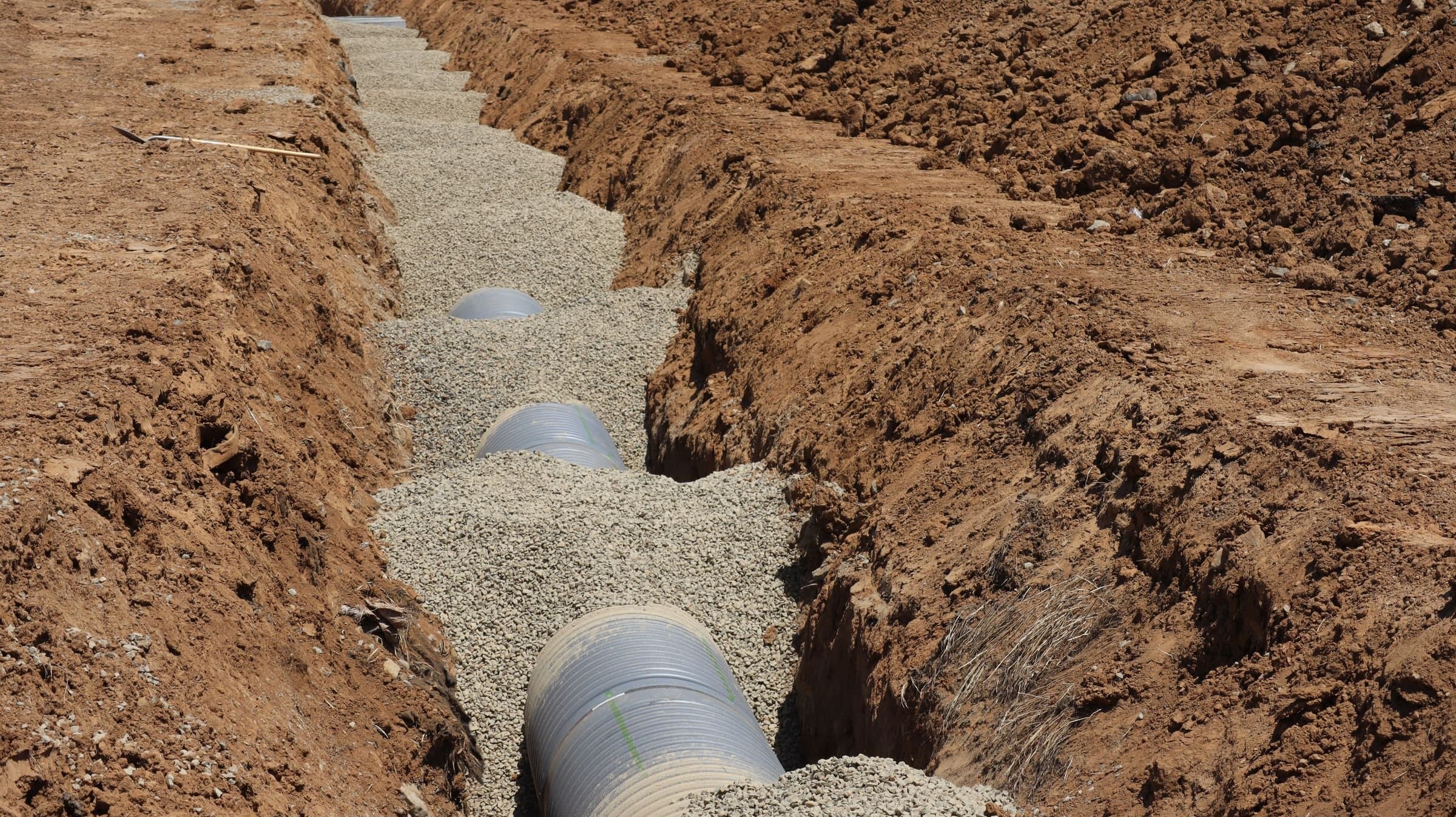 Drainage pipe bedded in gravel at the bottom of an open trench.